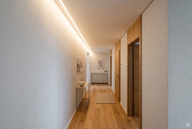 Schmaler Wohnflur mit warmem Lichtband an der Decke, Parkett und eleganter Konsole mit Deko-Vase.