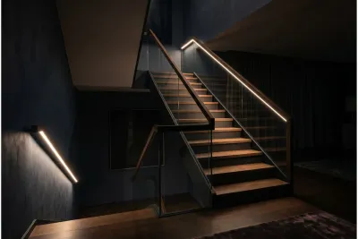 Homogene LED-Lichtlinie im Handlauf bei Nacht Stilvolle Innentreppe aus Holz und Glas in dunkler, edler Gesamttonalität bei Nacht. Eine durchgehende, warmweiße LED-Beleuchtung im Handlauf wirft ein sanftes, punktfreies Licht auf die Stufen.
